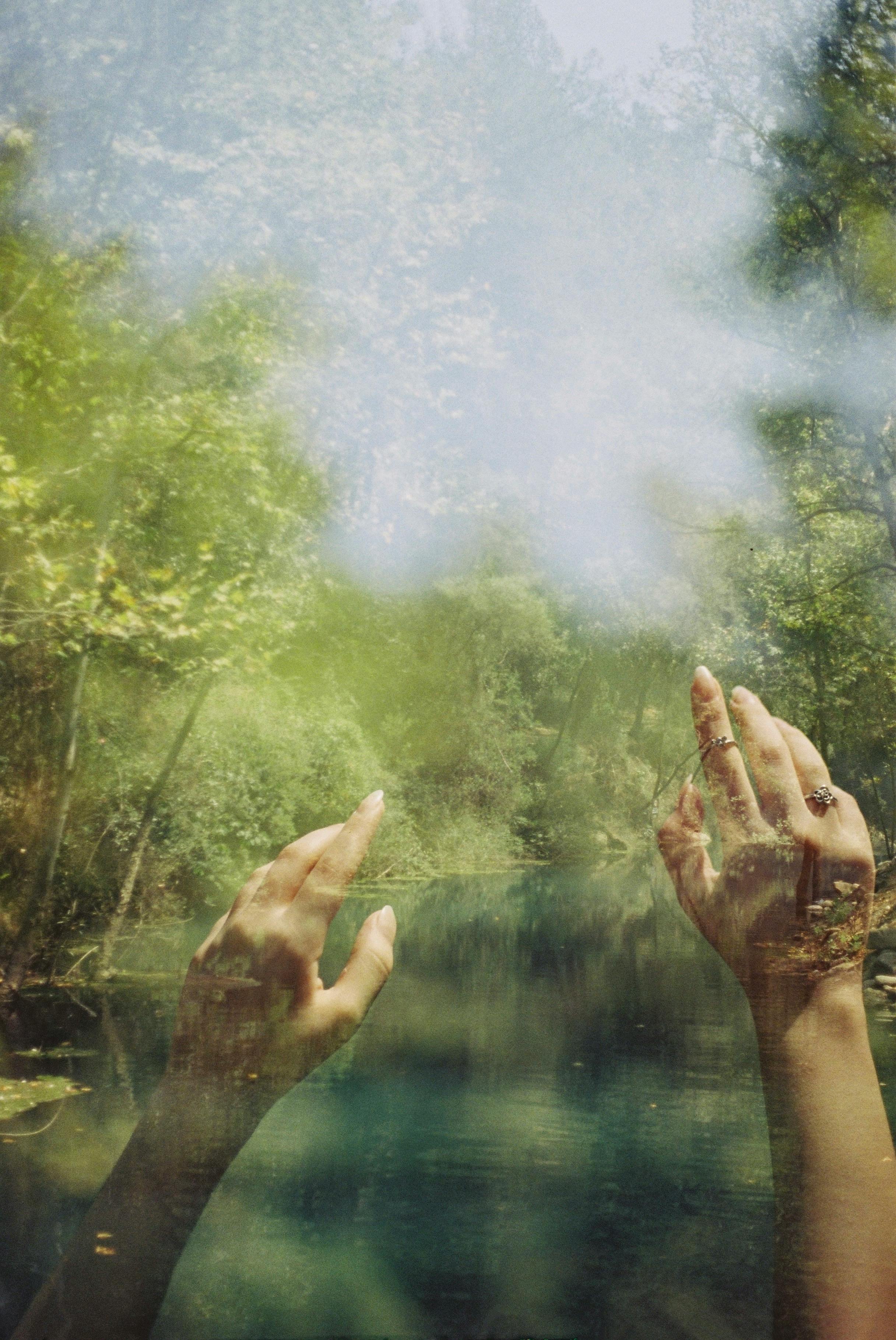 Double exposure of raised hands over a lush green forest and river scene